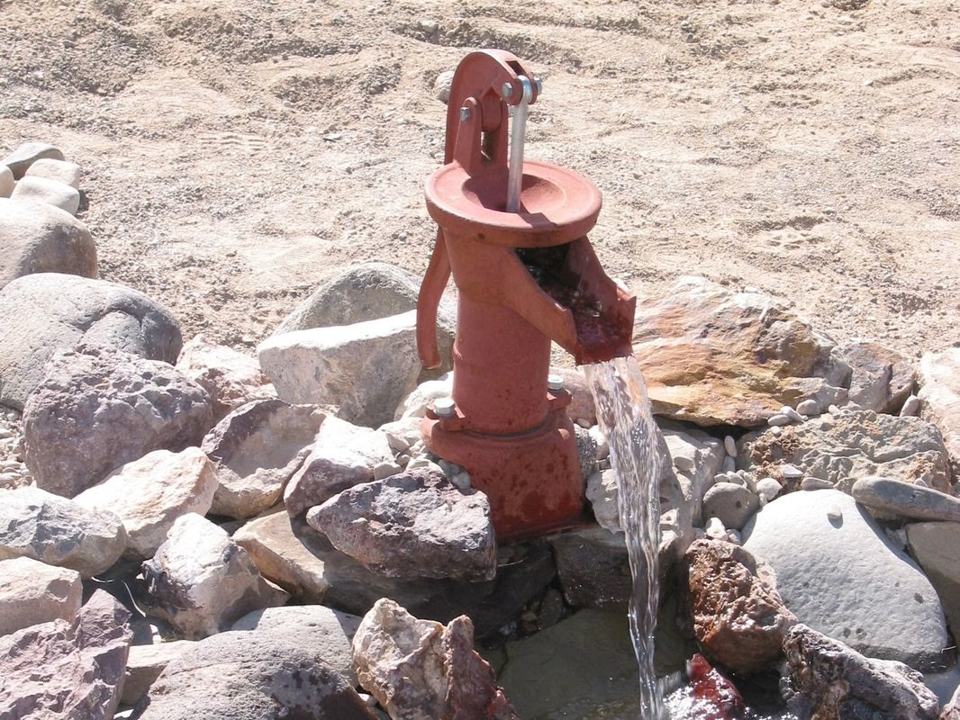 Red hand pump pouring into a rock water feature