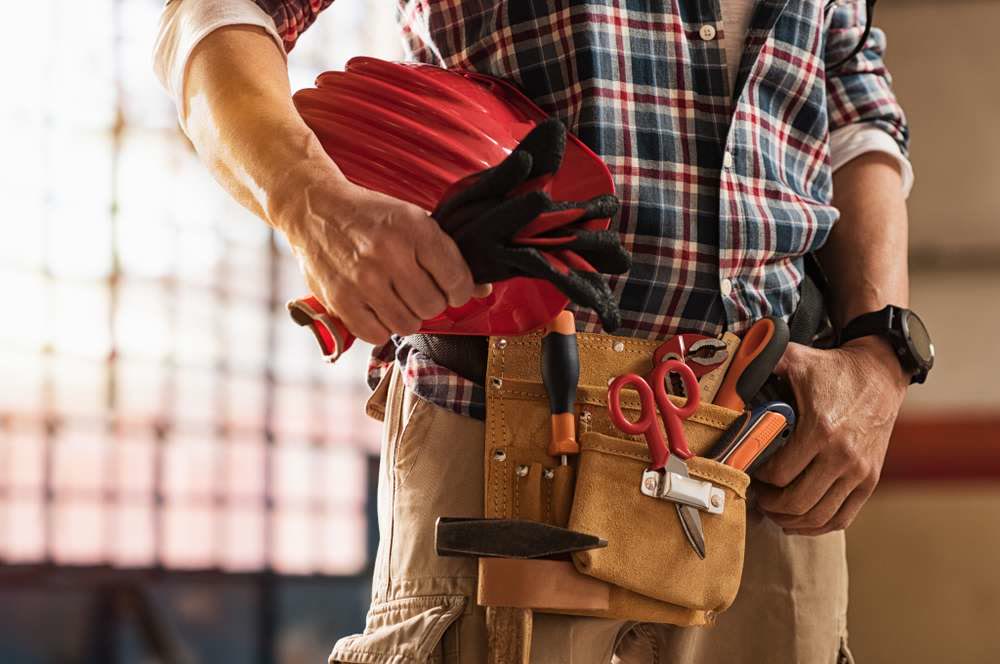 Handyman with a loaded tool belt, holding a hard hat and work gloves