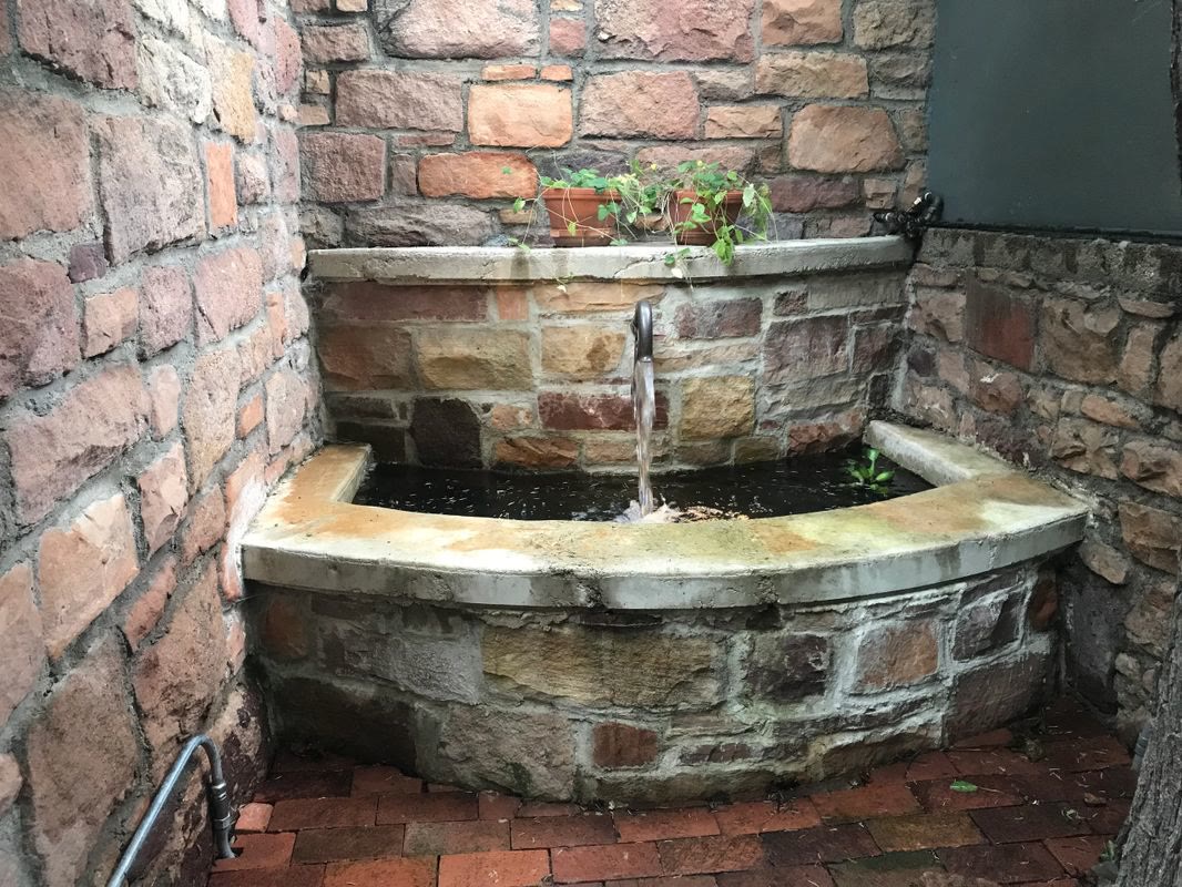 Stone wall fountain with water spilling into a basin